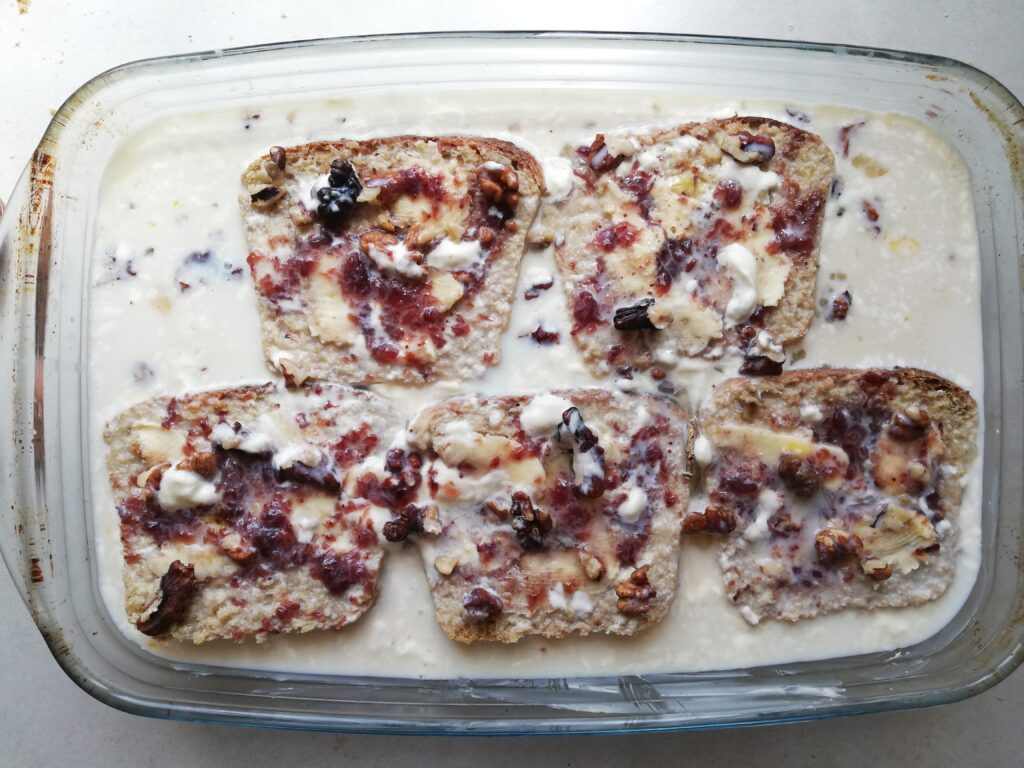 glass dish with slices of sourdough bread with butter and jam with mixed eggs, cream and milk poured around it