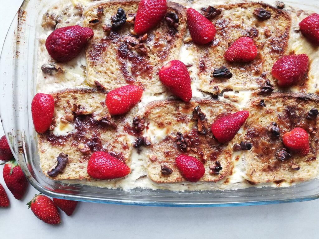 glass dish with sourdough strawberry French toast casserole with walnut pieces and fresh strawberries on top