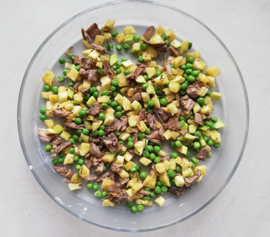 round glass pie dish with cubed courgettes, peas and shredded beef