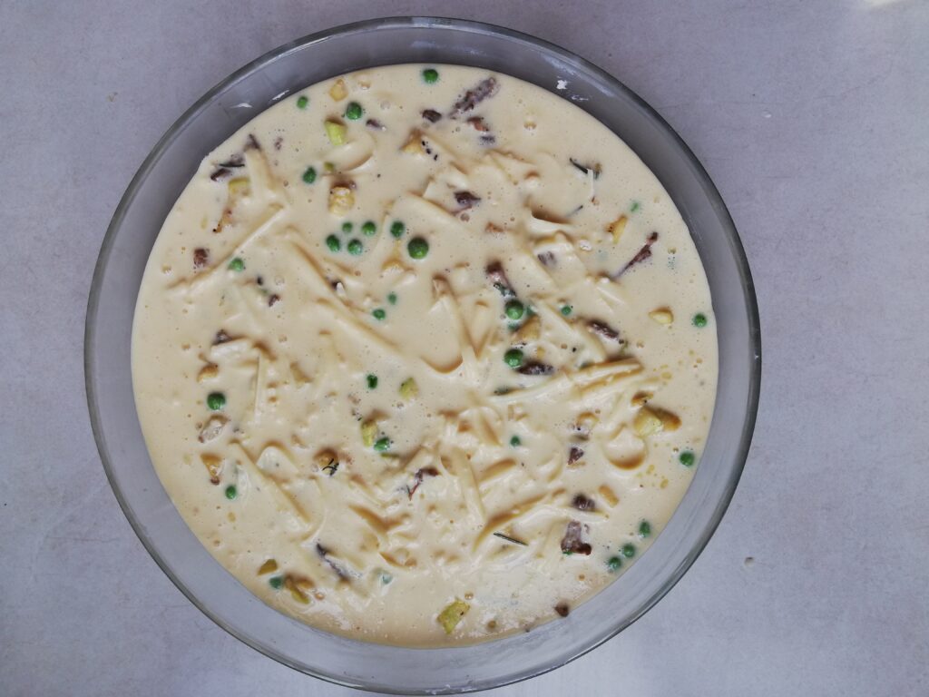 round pie dish with unbaked crustless quiche with shredded cheese on top