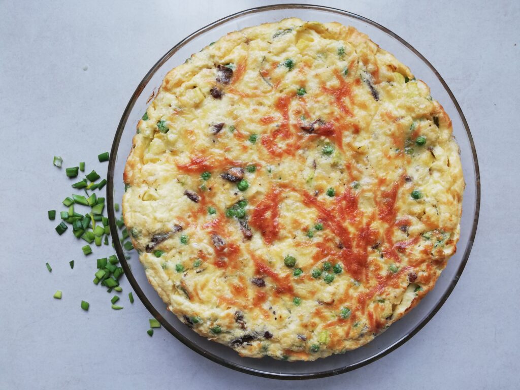 round pie dish with crustless quiche with peas, courgette and shredded beef with chives scattered on the side