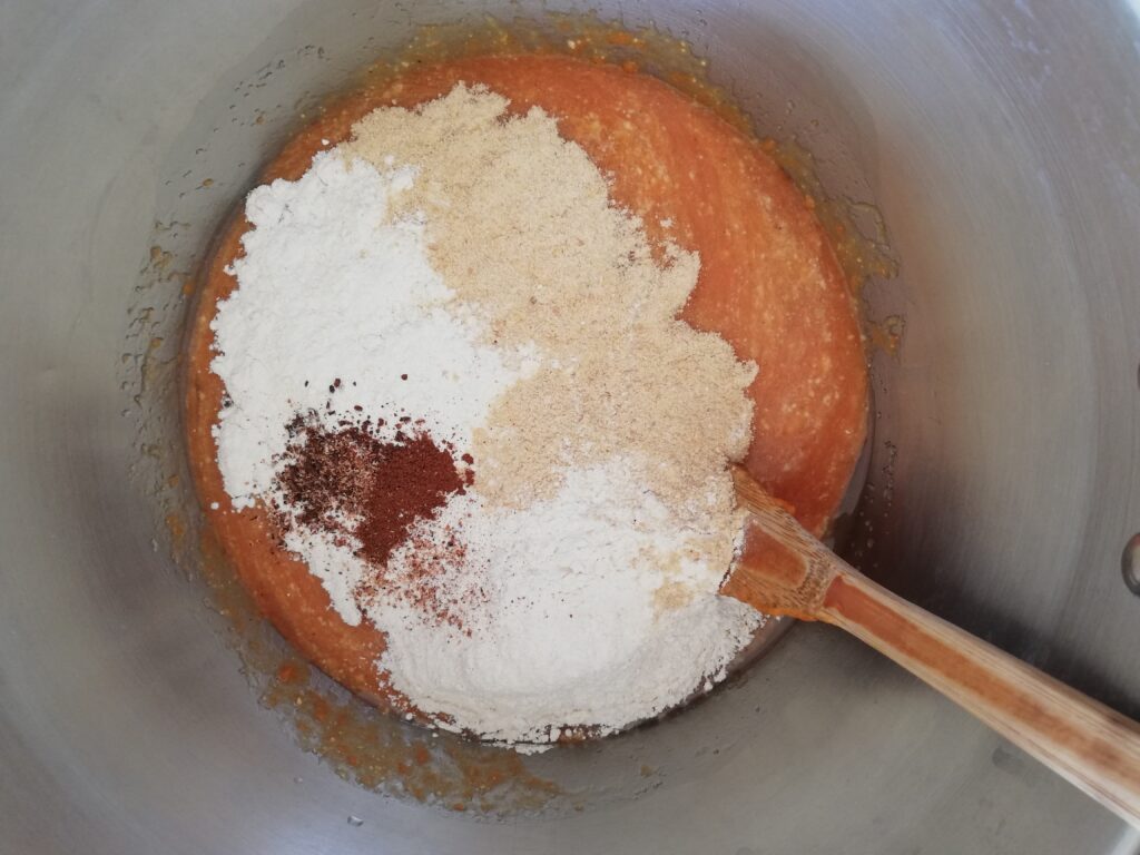 a metal bowl with pumpkin puree oil eggs white flour whole wheat flour pumpkin spices and a wooden spoon