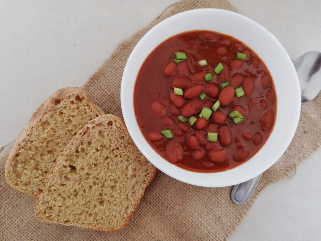 a bowl of baked beans garnished with green onions with two slices of sourdough bread and a metal spoon