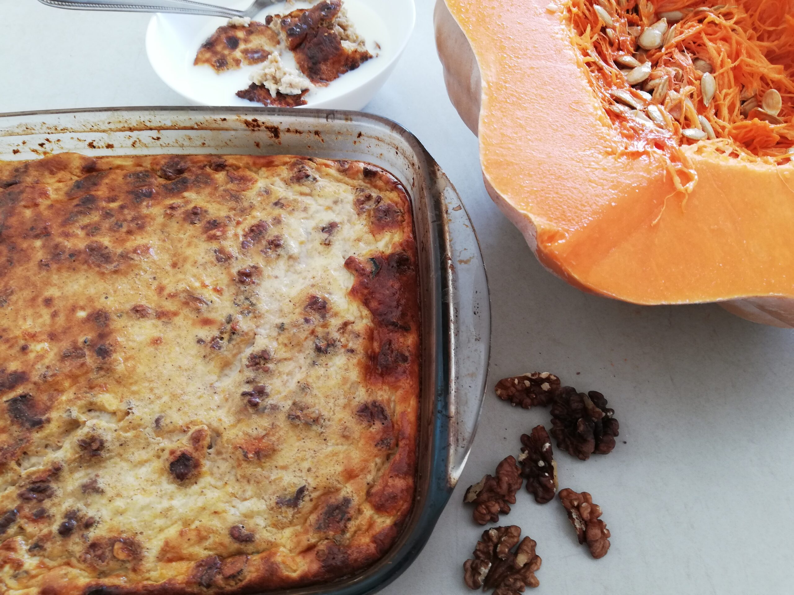 a casserole dish with pumpkin baked oatmeal a bowl of baked oatmeal with milk a large slice of pumpkin and some walnut pieces