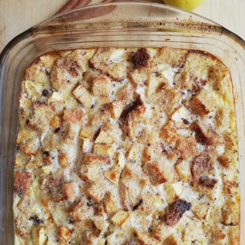 glass casserole dish with sourdough apple cinnamon baked french toast with an apple and two cinnamon sticks on the side