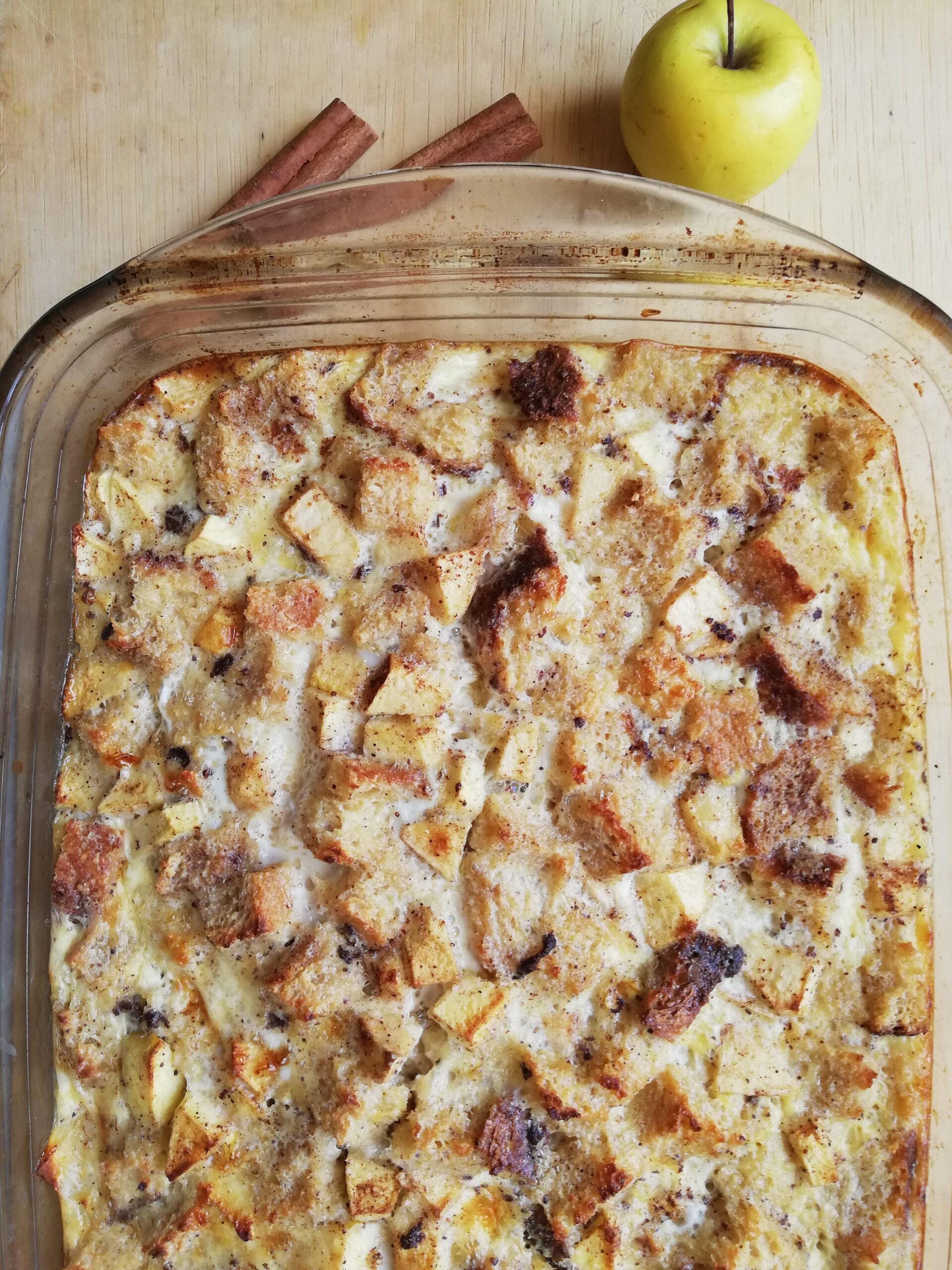 glass casserole dish with sourdough apple cinnamon baked french toast with an apple and two cinnamon sticks on the side