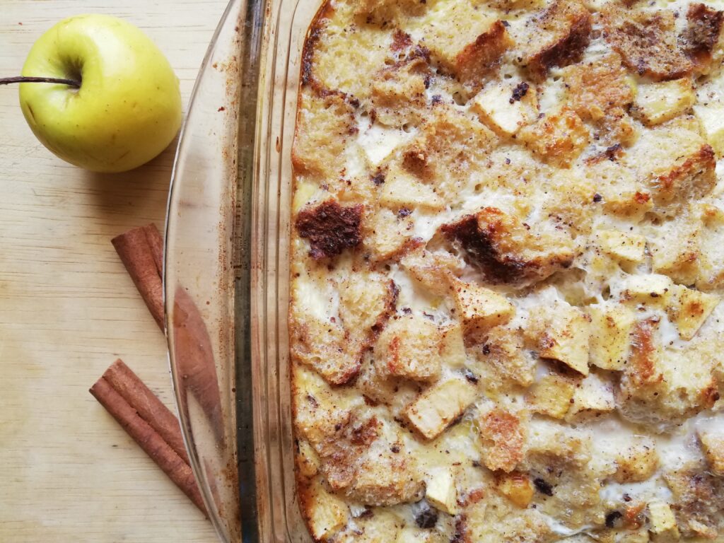 glass dish with sourdough apple cinnamon baked french toast with and apple and two cinnamon sticks on the side