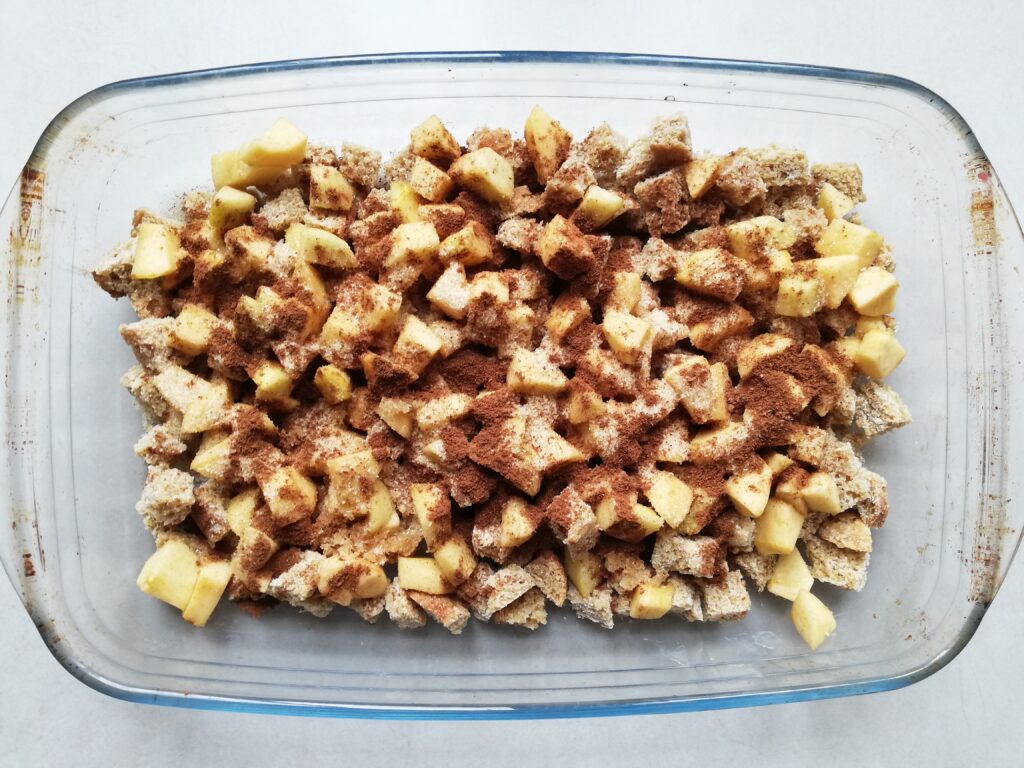 glass casserole with cubed bread and chopped apples with cinnamon sprinkled on top