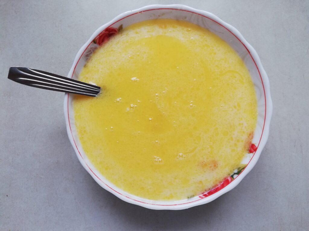 large bowl with whisked eggs, milk and butter with a metal fork.