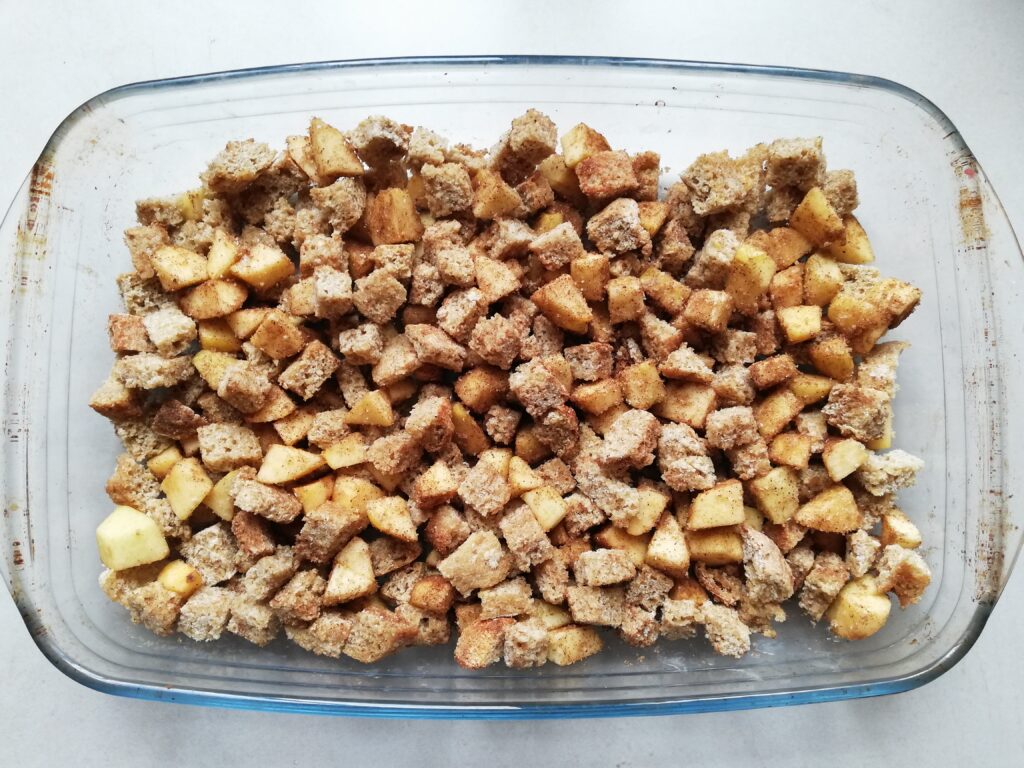 glass casserole with cubed bread chopped apples and cinnamon mixed together