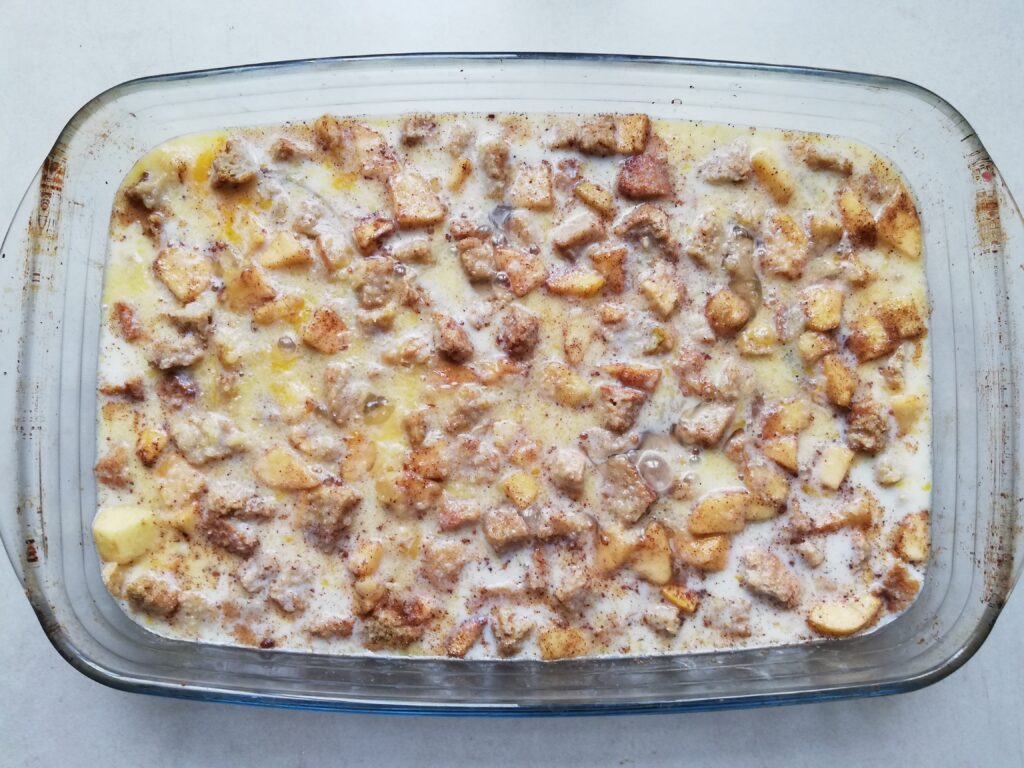 cubed bread and apples with milk and melted butter in a glass casserole dish