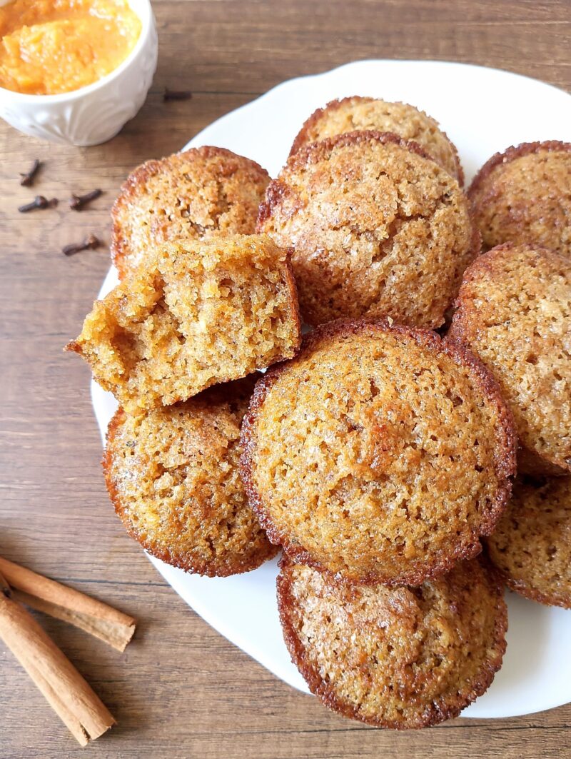 Sourdough pumpkin muffins on plate with a cup of pumpkin puree and cinnamon sticks on the side