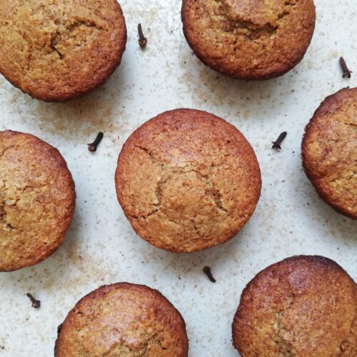 Sourdough gingerbread muffins on a counter top with brown sugar and cloves sprinkled around