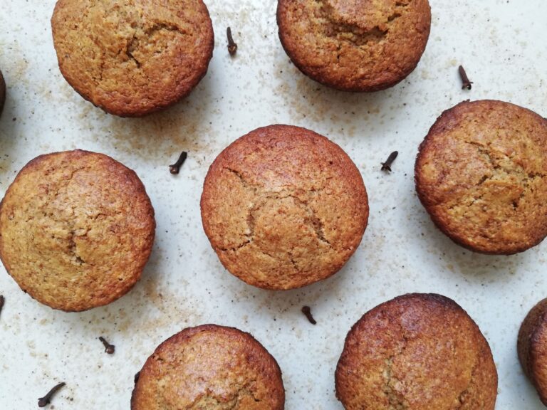 Sourdough gingerbread muffins on a counter top with brown sugar and cloves sprinkled around