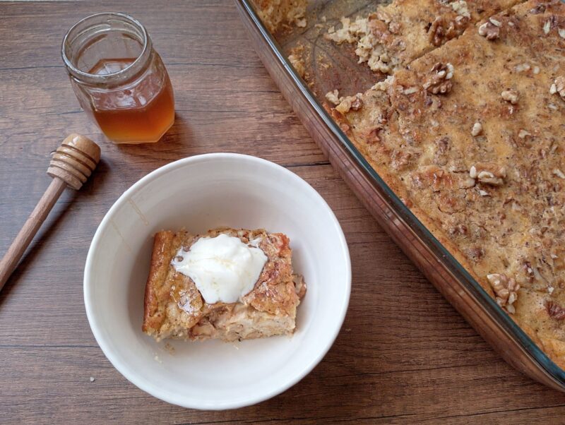 Slice of pumpkin baked oatmeal in bowl with a dollop of cream and baking dish with baked oatmeal on the side