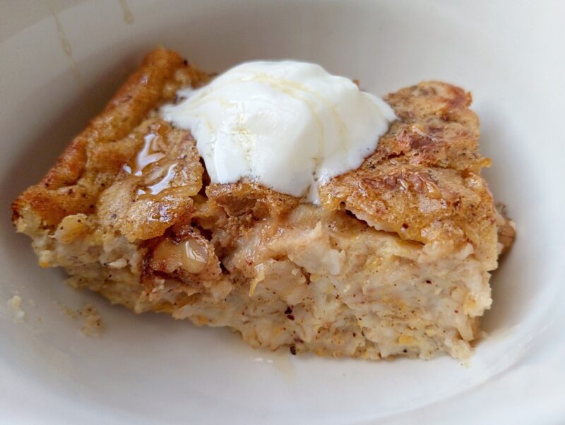 Slice of pumpkin baked oatmeal in bowl topped with cream and drizzled with honey