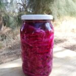 a jar of red cabbage sauerkraut with orange and cloves on a wooden tray with trees in the background