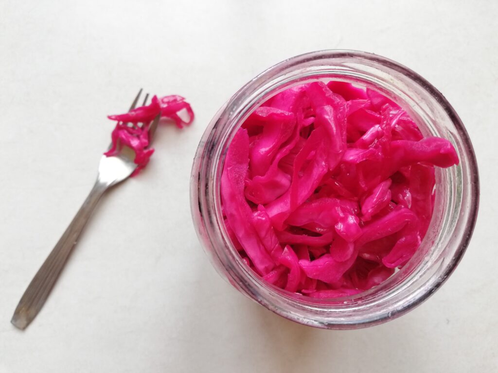 a jar of red cabbage sauerkraut with orange and cloves and a fork with some of the sauerkraut on it