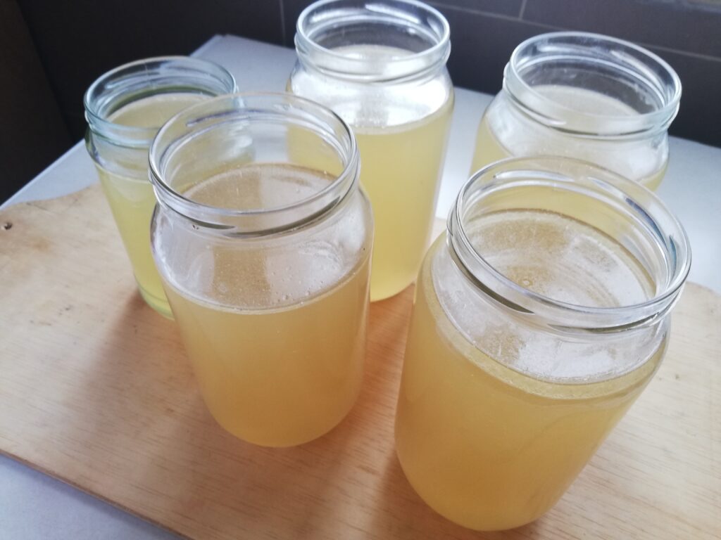 five jars of old hen broth standing on a wooden tray.