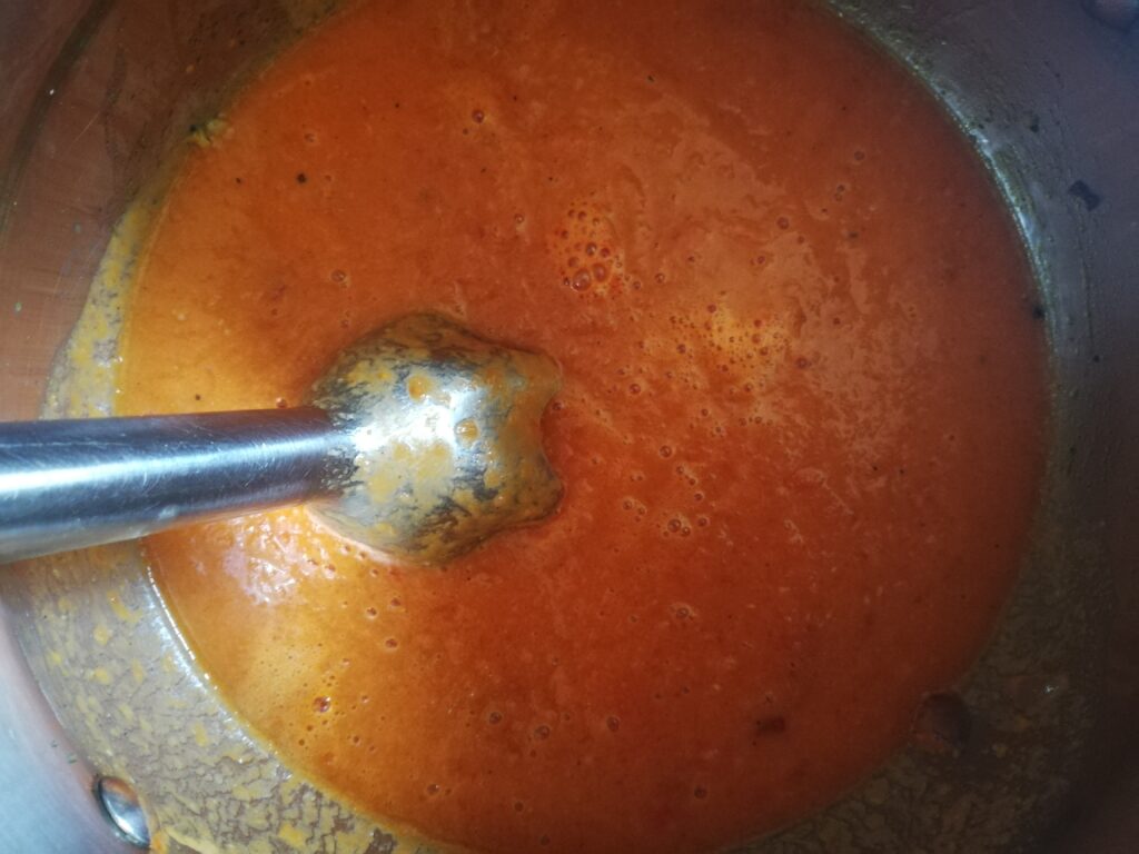 blended tomatoes and stock in a metal pot with the stick blender on the side