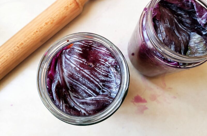 Adding folded cabbage leaf on top of shredded salted red cabbage in jar