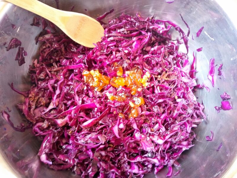 Adding ground cloves and some orange marmalade to a bowl of shredded red cabbage