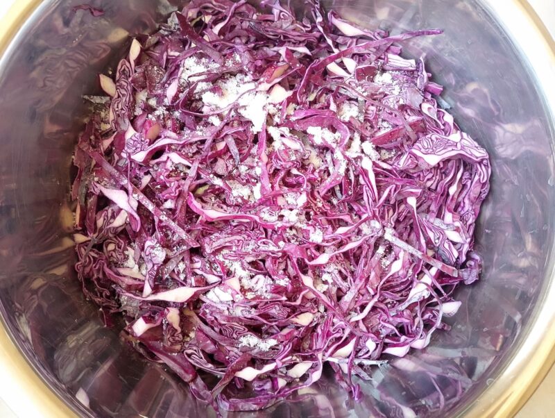 Adding salt to a large bowl full of shredded red cabbage