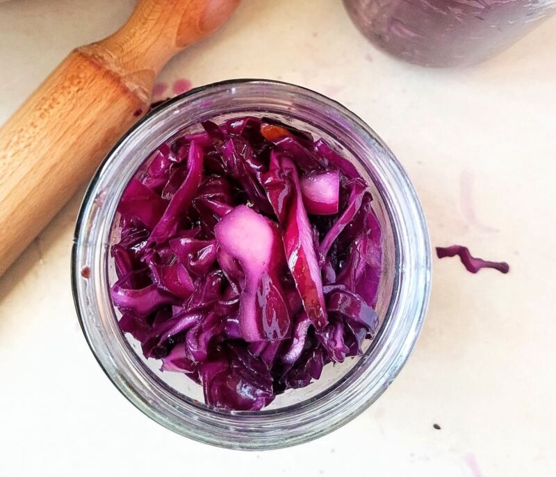 Packing red cabbage into jars using flat end of rolling pin
