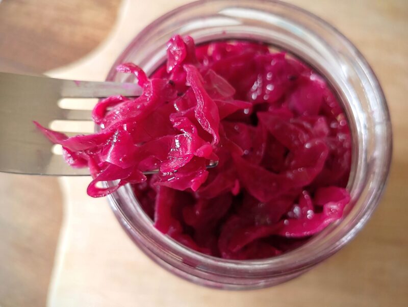 Fork lifting some red cabbage sauerkraut out of the jar