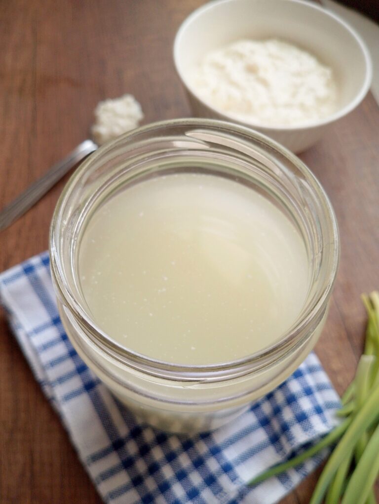 What to do with leftover whey: jar of whey on wooden table with a bowl of cottage cheese nearby