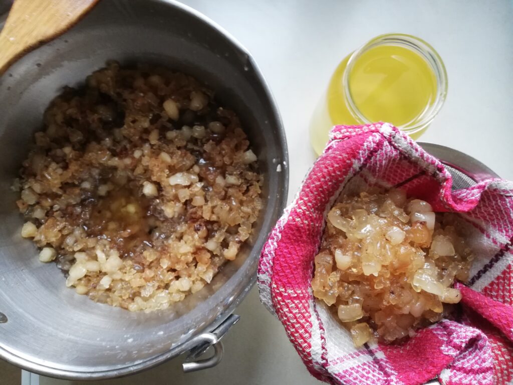 a large pot with rendered tallow and cracklings a sieve lined with a kitchen towel with cracklings in it and a jar of melted tallow