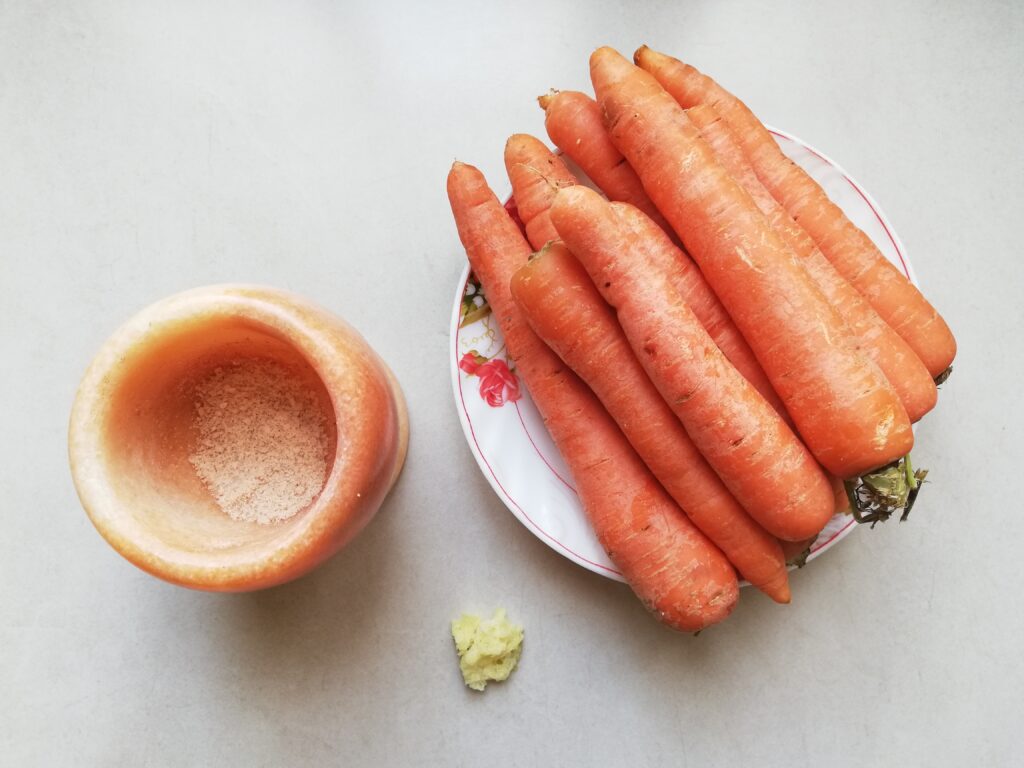 a mortar with unrefined salt a plate piled with carrots and fresh grated ginger on a marble counter top