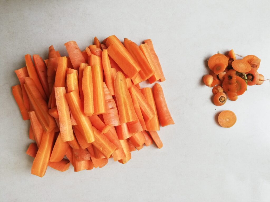 a large pile of carrot sticks on the left and cut off carrot tops on the right