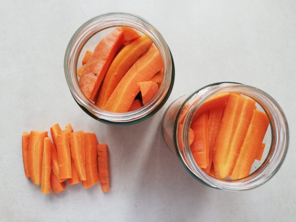 two canning jars full of carrot sticks and a small pile of carrot sticks on the left