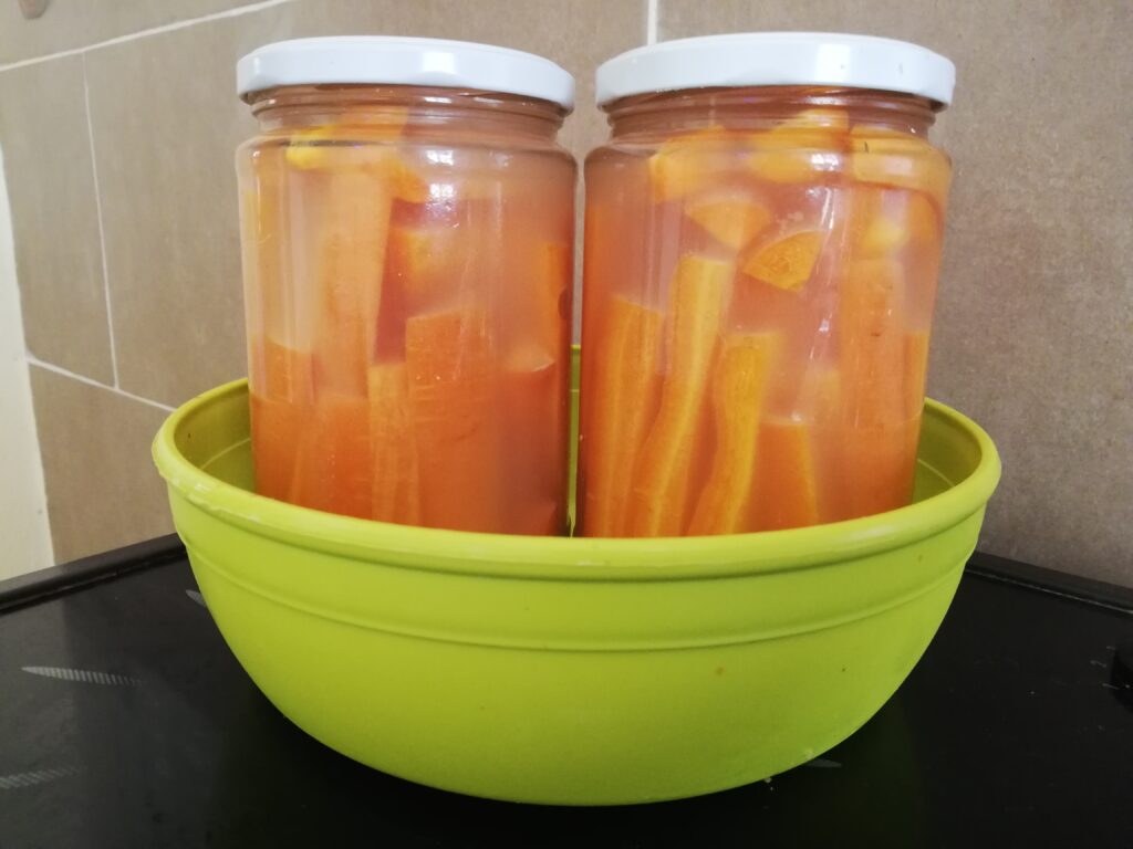 two jars with lacto fermented carrots with ginger standing in a green plastic bowl