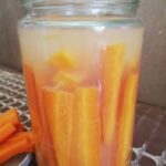 a jar of lacto fermented carrots with ginger with some fermented carrots sticks on the side