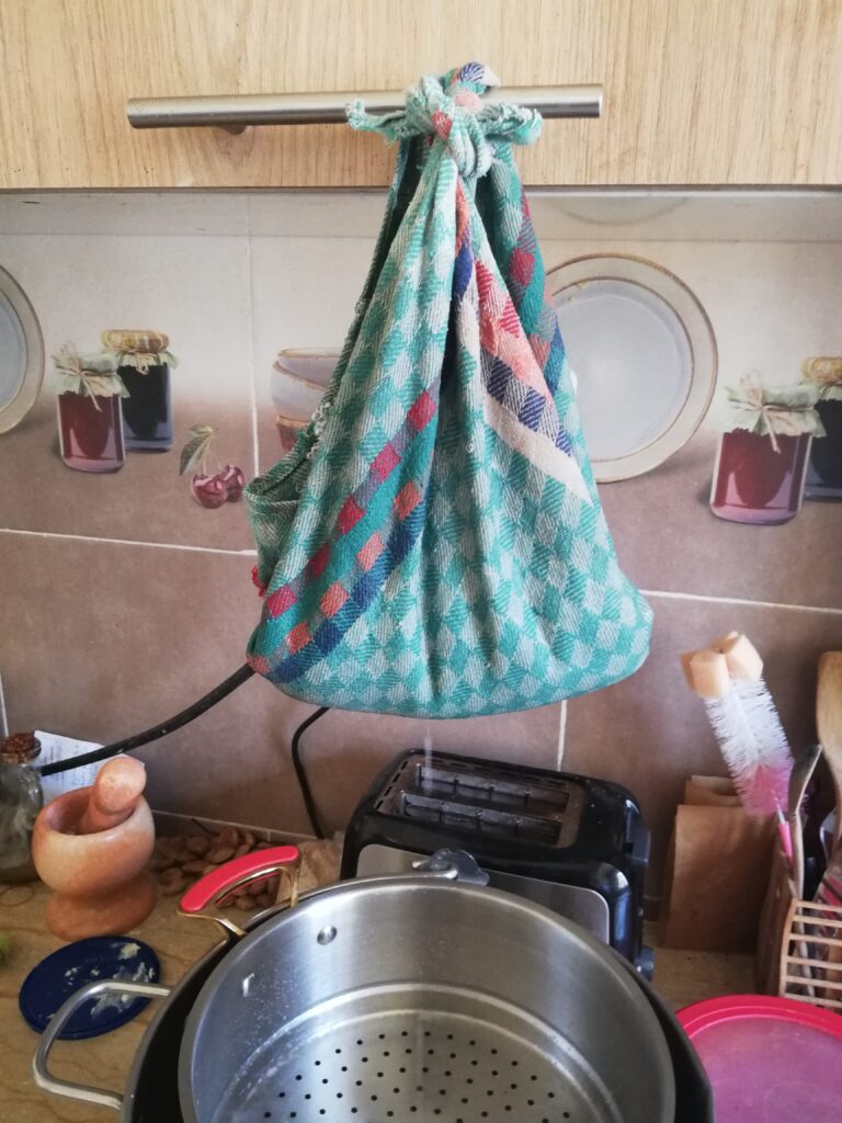 homemade cottage cheese tied in a tea towel and draining over a large colander