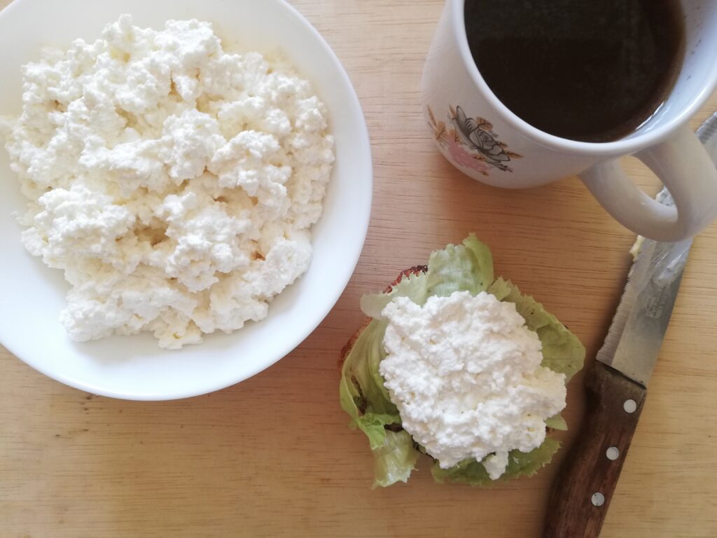 a white bowl with cottage cheese a mug of tea a slice of sourdough bread with lettuce and cottage cheese and a buttered bread knife