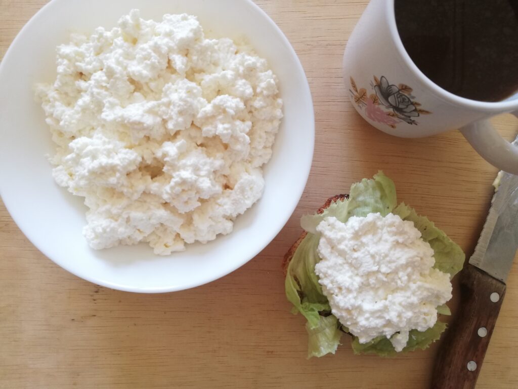a white bowl of cottage cheese a mug of tea a slice of sourdough bread with lettuce and cottage cheese and a bread knife