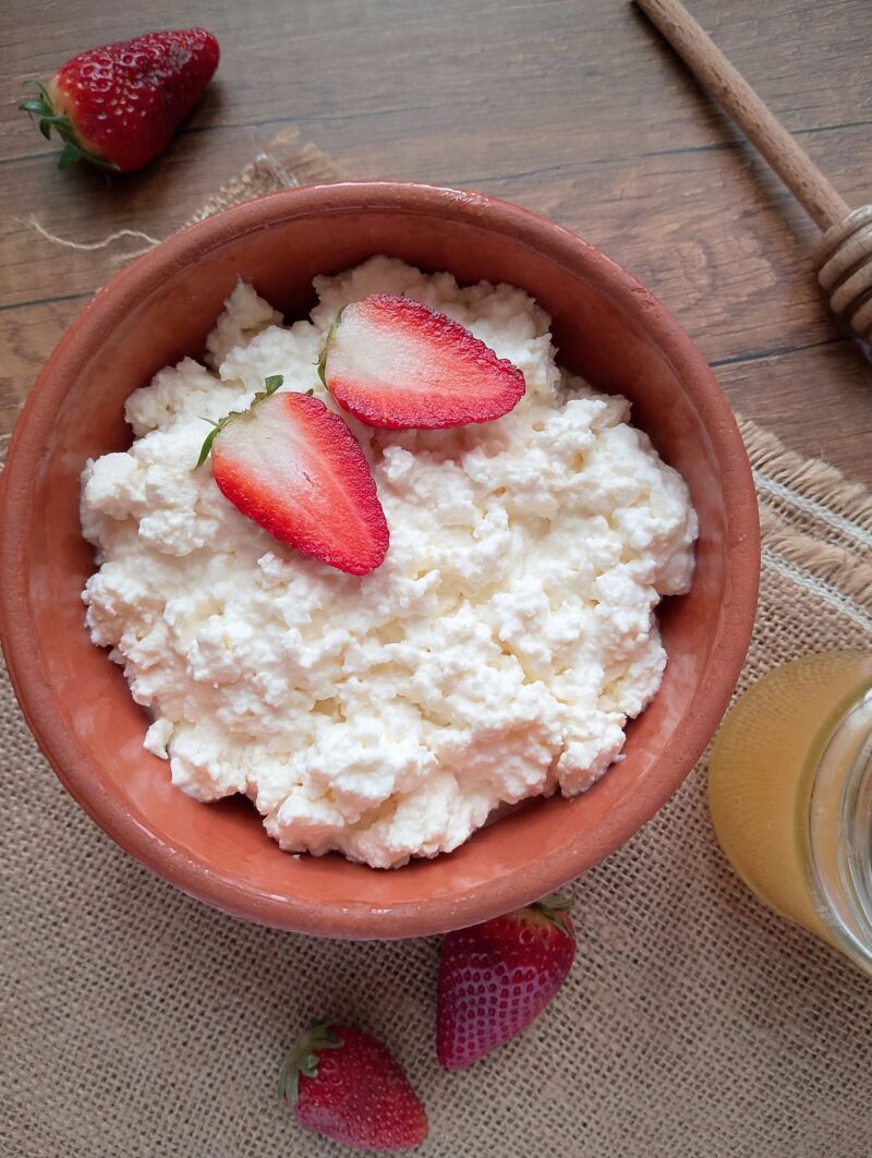 Raw milk cottage cheese in bowl with fresh strawberries and honey on the side
