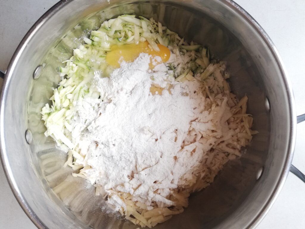 a large metal pot with grated potatoes grated zucchini egg white flour and salt
