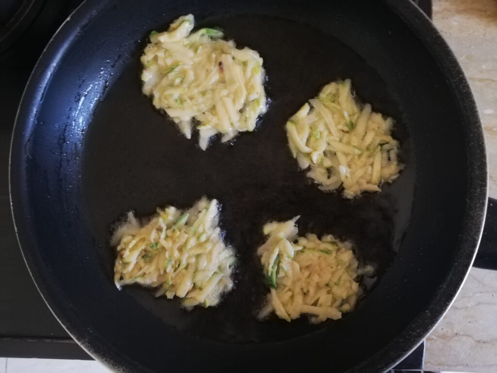 four zucchini and potato fritters cooking in a frying pan