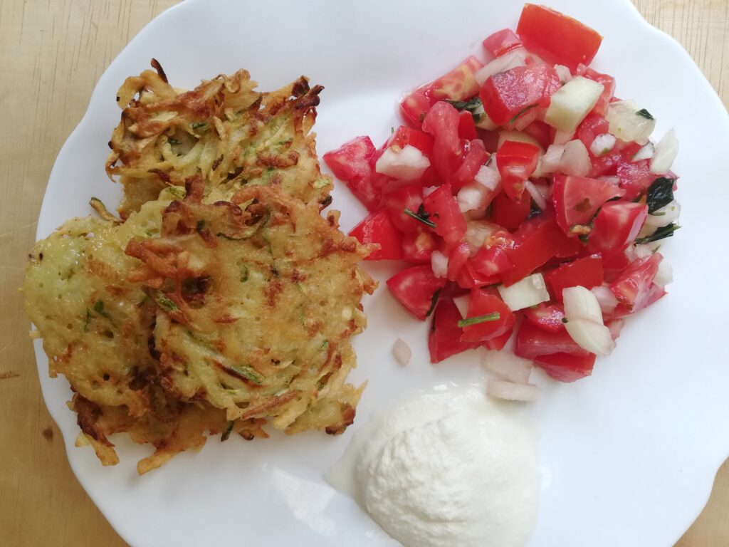 white plate with zucchini and potato fritters salsa and a dollop of sour cream