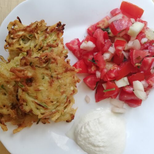 white plat with zucchini potato fritters salsa and a dollop of sour cream