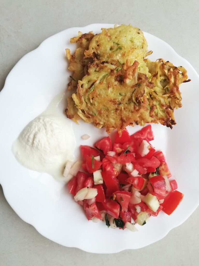 a white plate with some zucchini and potato fritters salsa and a dollop of sour cream