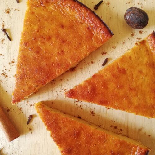 three slices of pumpkin pie on a wooden board with spices and brown sugar around