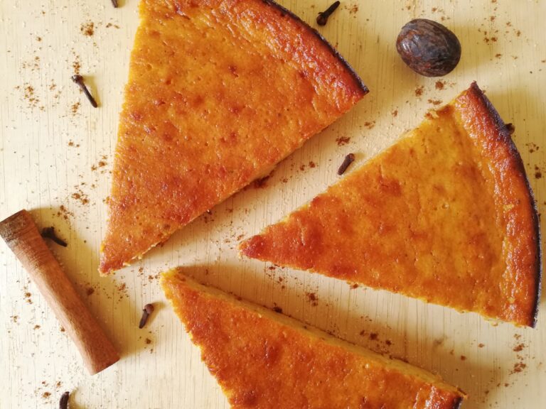 three slices of pumpkin pie on a wooden board with spices and brown sugar around