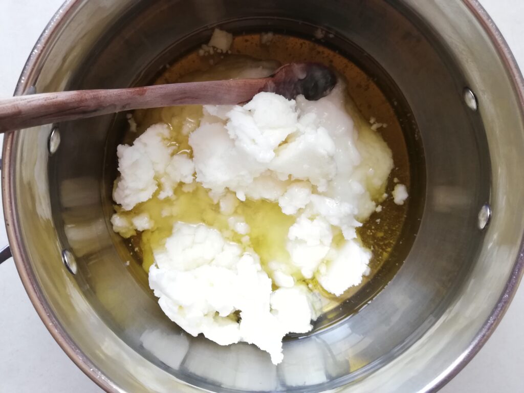 large metal pot with coconut oil tallow olive oil and castor oil with a wooden spoon on the side