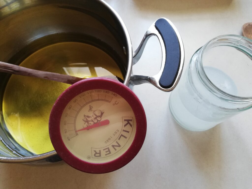 pot with melted fats and oils and a thermometer inserted in them on the left a jar with lye water on the right