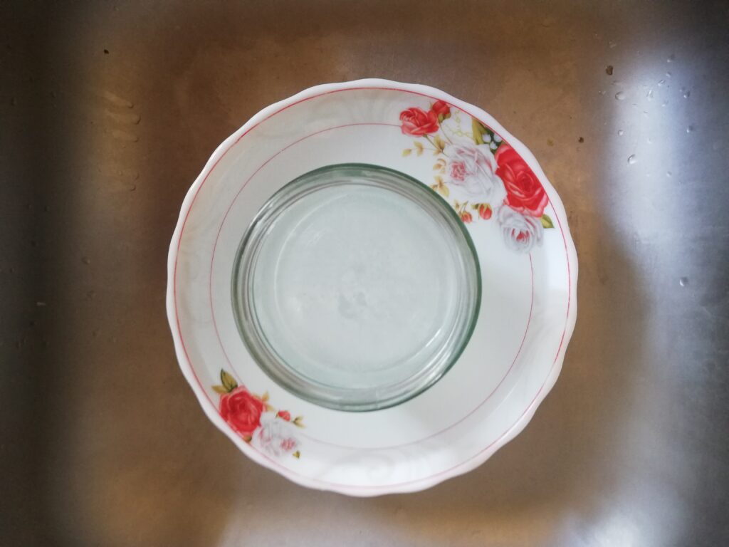 a jar of lye solution in a bowl filled with water placed in the kitchen sink
